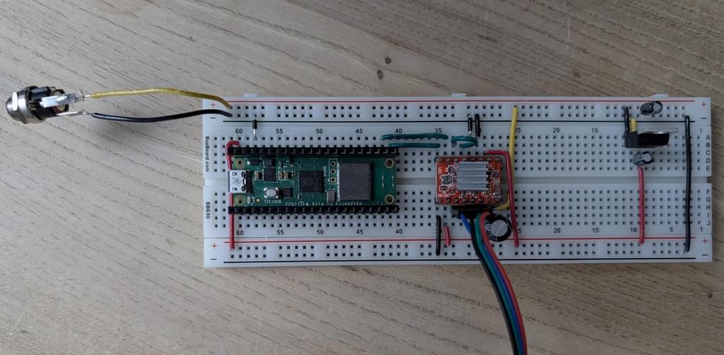 Breadboard with a barrel jack connected to the power rails on flying leads. From left to right there's a Raspberry Pi Pico W, A4988 stepper motor driver and L78 series linear regulator.